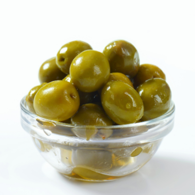 Cuenco de vidrio con aceitunas verdes aliñadas sobre fondo blanco