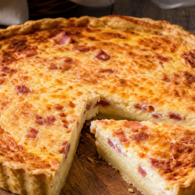 Quiche lorraine tradicional recién horneada sobre tabla de madera, con una porción servida mostrando su relleno cremoso de inspiración francesa