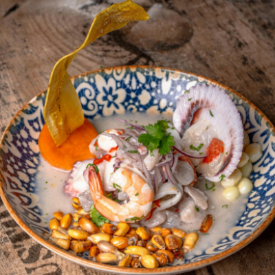 Ceviche peruano con pescado y marisco, cebolla roja, cilantro, maíz tostado y plátano crujiente, servido en un cuenco decorado.